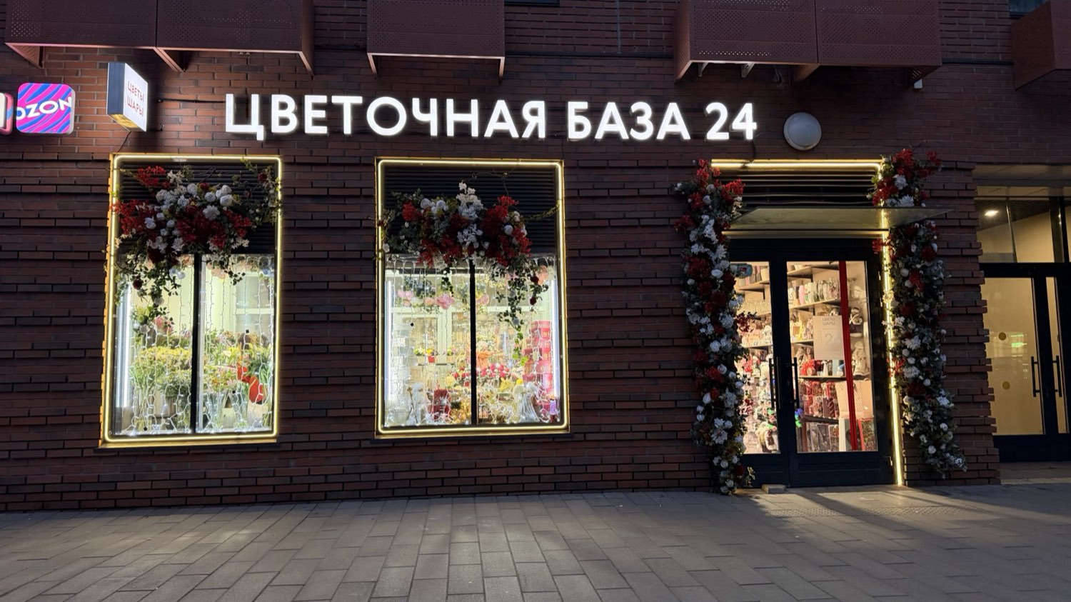 Цветочная база 24 в Москве вечером: золотистый LED контур вокруг двух витрин и входной группы, кирпичный фасад, BossDiodov